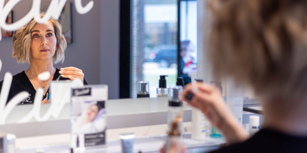 Ethetician reflected in mirror while applying a serum
