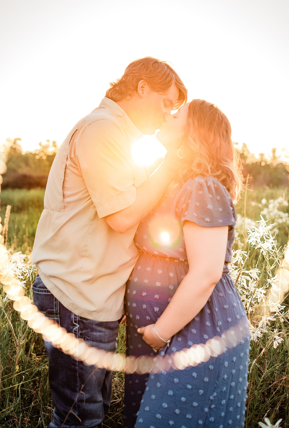 A married couple kiss as the sun shines brightly behind them.
