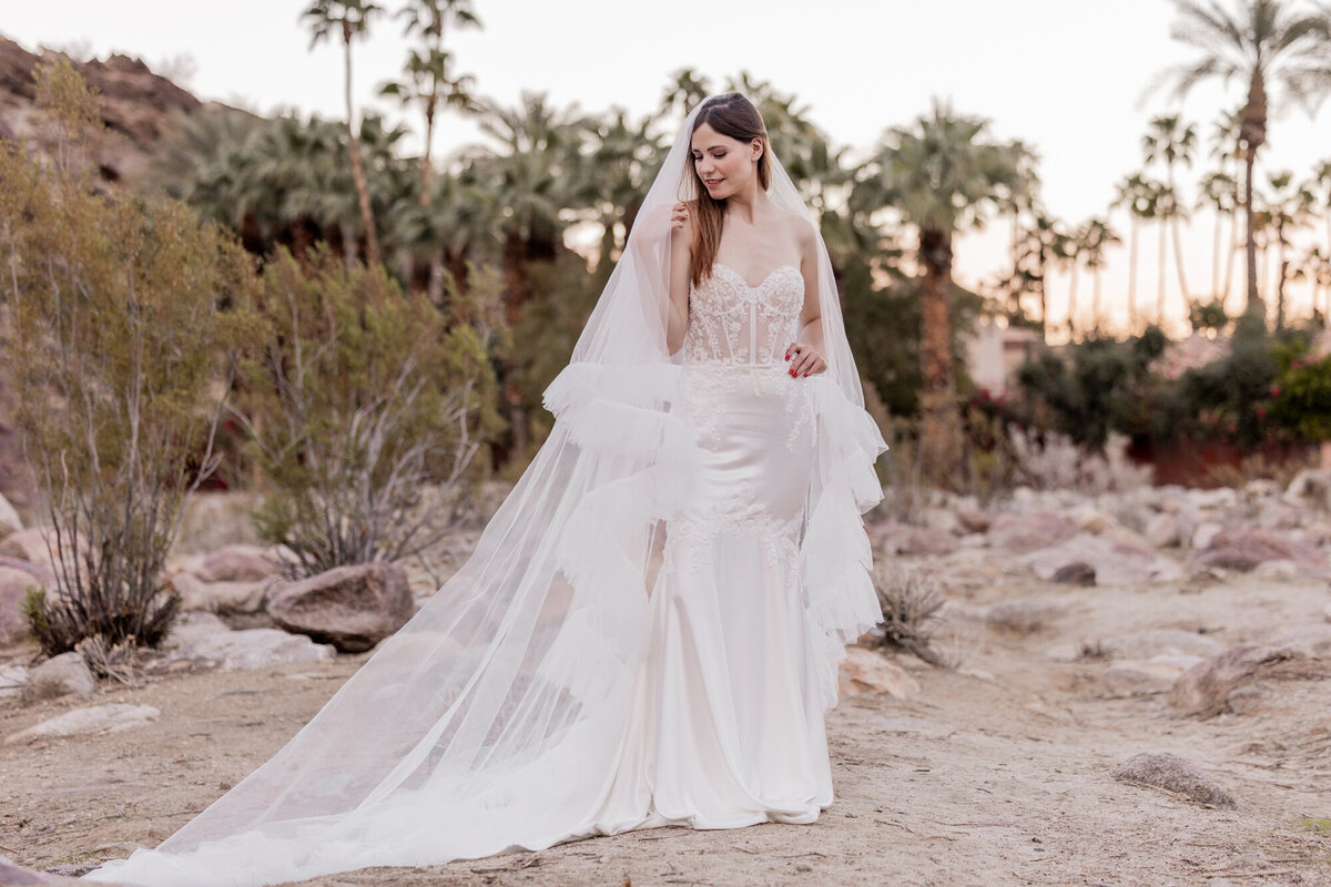 Bride walking across rocky terrain in lace gown and cathedral veil.