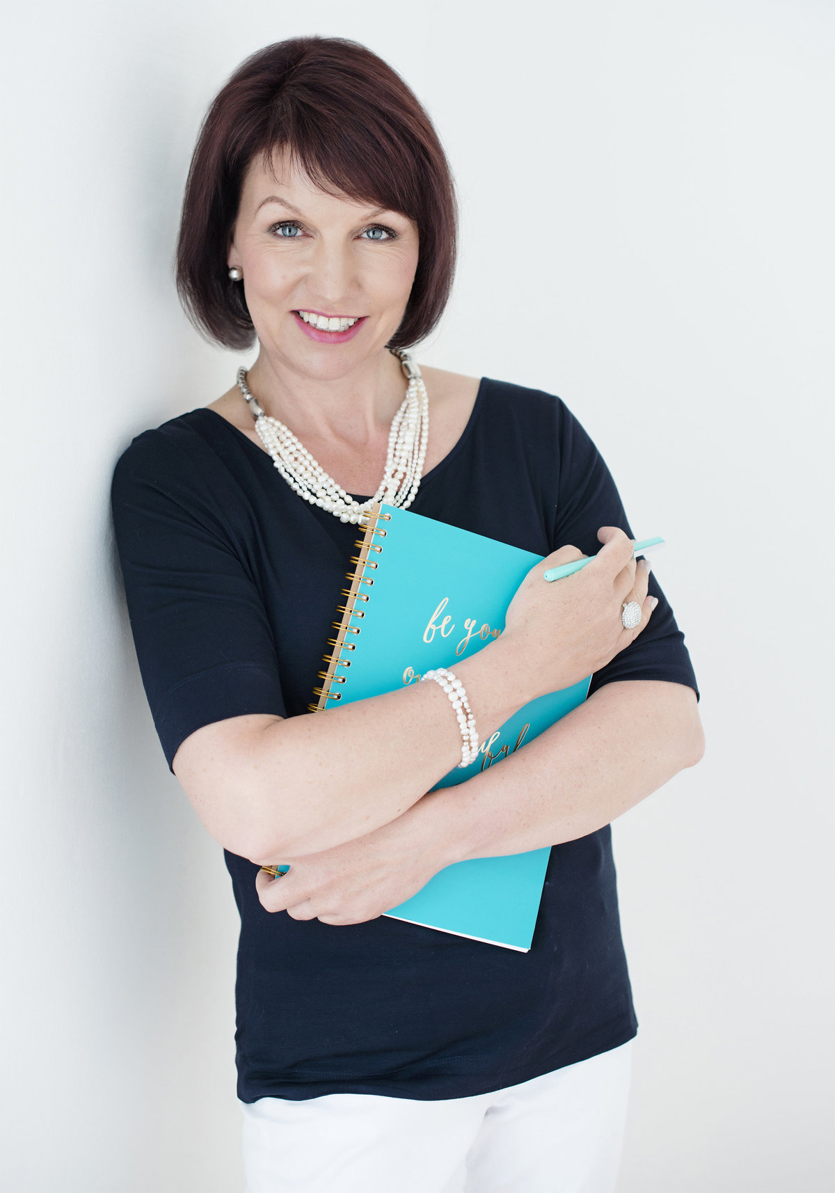 professional  woman portrait by puja  misra  of  zoom into life  studio , very  confident looking into camera holding a note book in her hand   and  wearing perl jewellery and  holding a pen inher hand