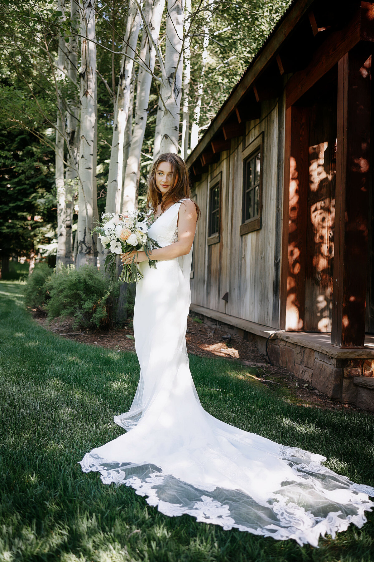 A solo portrait of a beautiful bride wearing her white dress, with lace on the train in their Aspen wedding,
