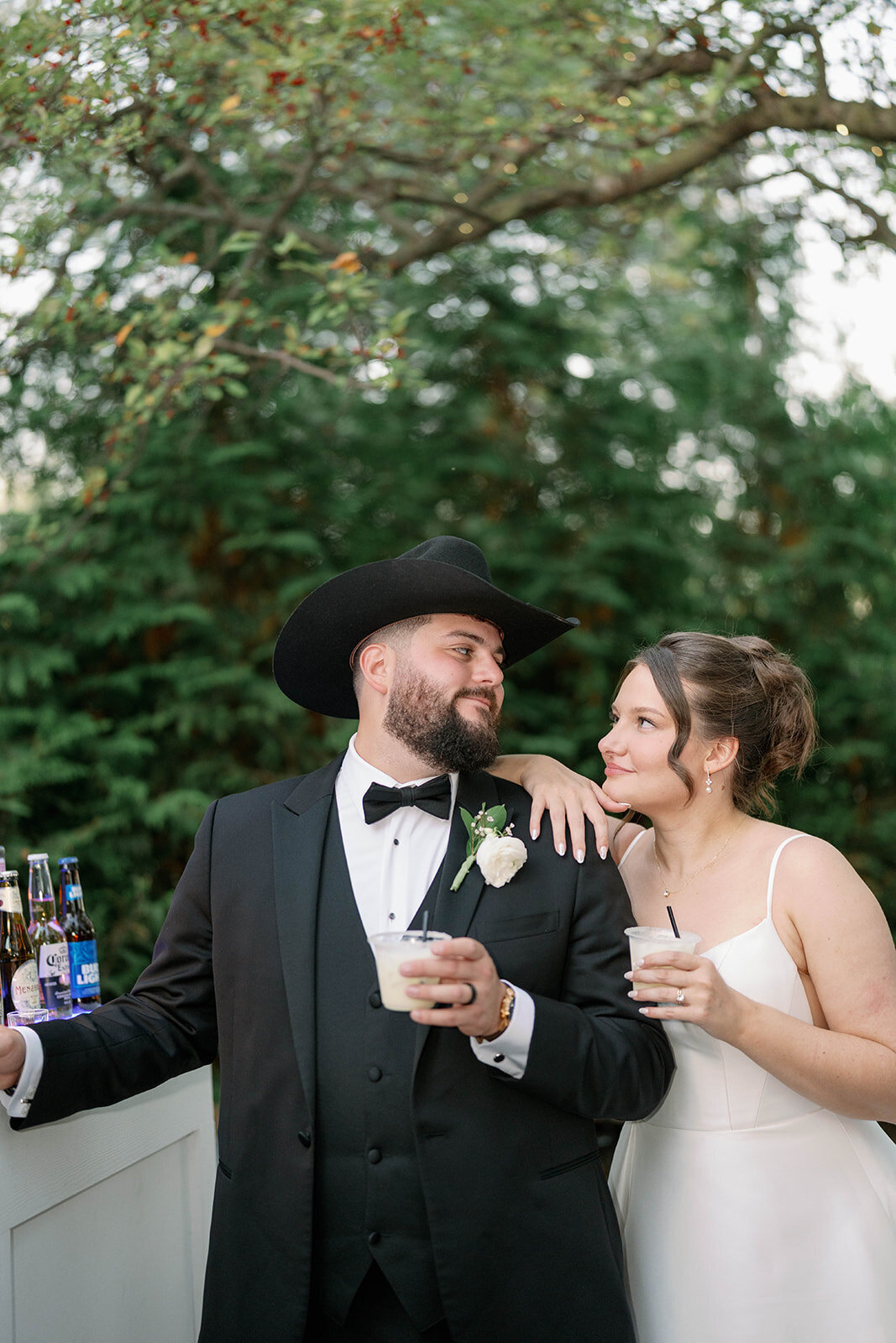 Bride and groom sharing cocktails and laughing at an outdoor bar during their Café Cortina cocktail hour in Dearborn Michigan.