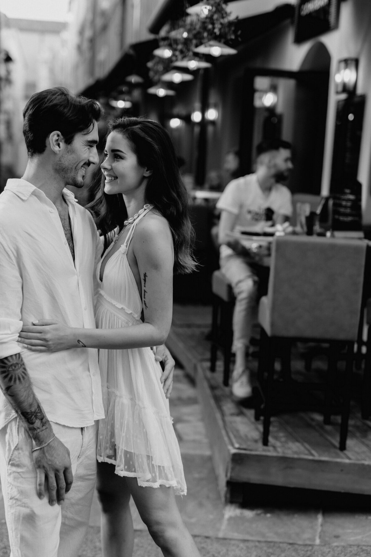 Engaged Couple turned towards one another and smiling outside of a cafe in Saint Tropez France.