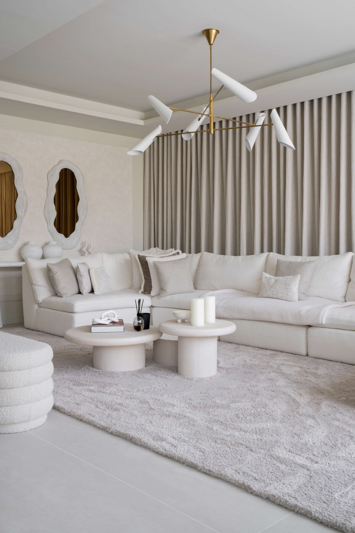 Spacious, modern living area with a large white sectional and white center table. Behind the couch is a white console table and two contemporary white mirrors.