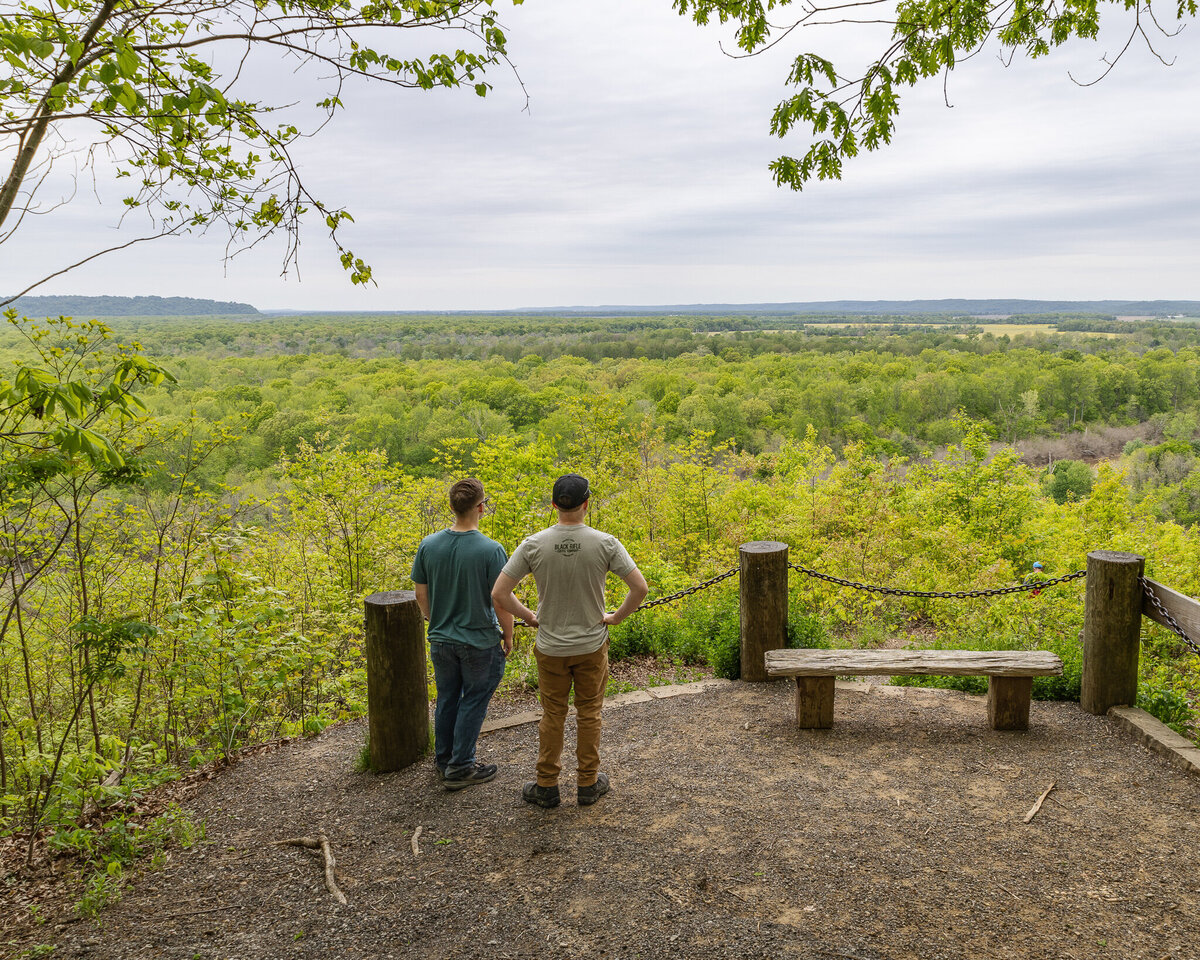 two adult brothers standing over a look out, looking at the view of trees as far as you can see
