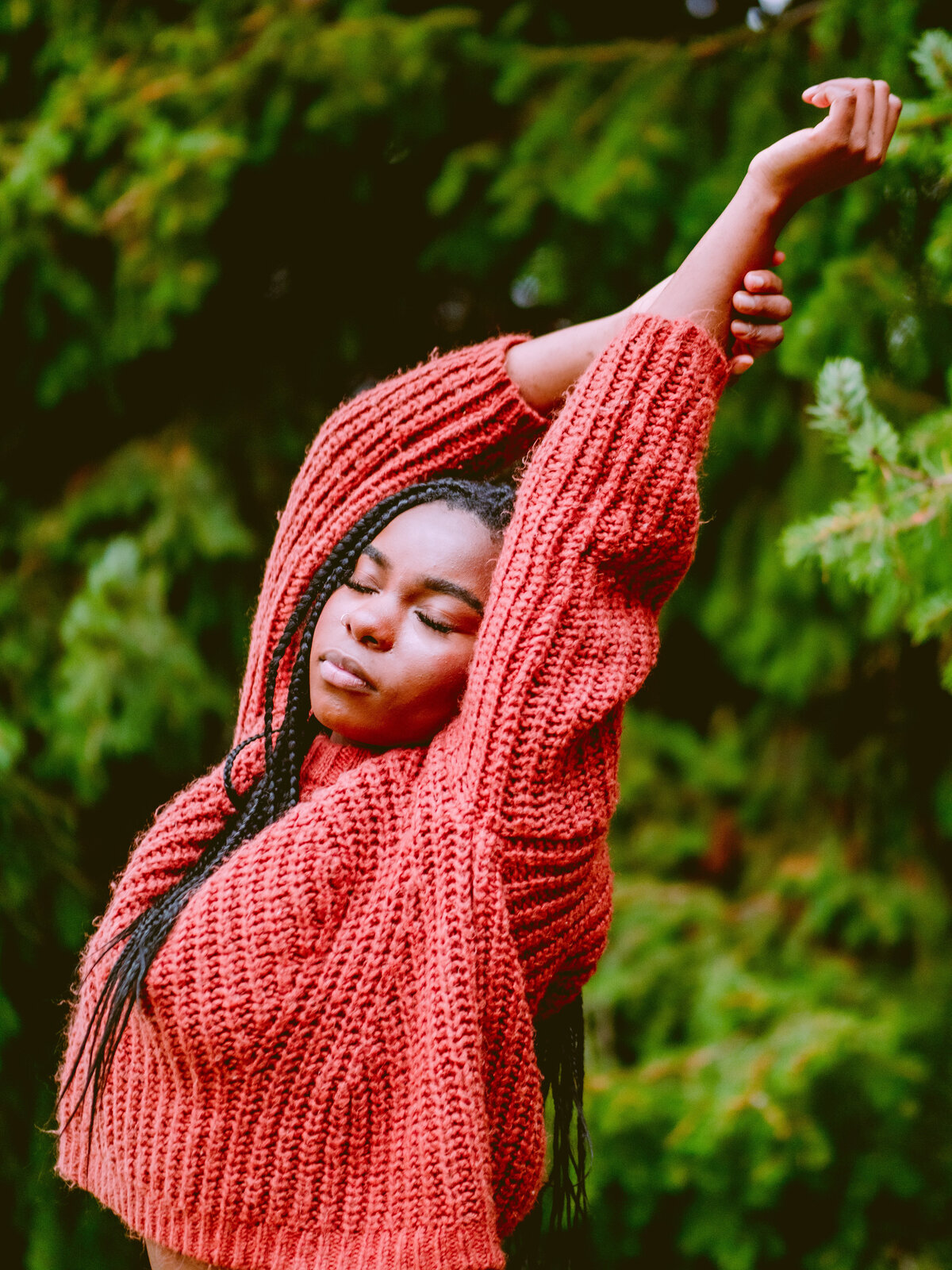 Portrait of a creative woman in a red sweater with arm raised, surrounded by greenery – expressive brand photo by Mewphotovideo