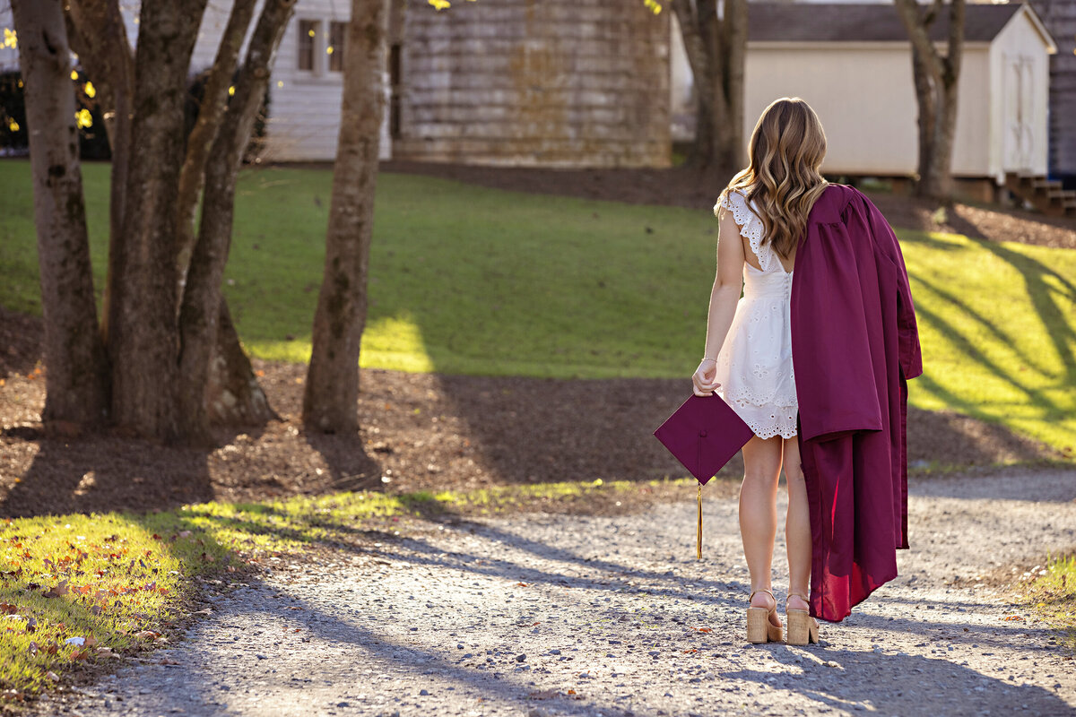 High school senior in cap and gown standing in wooded area with rustic fall backdrop