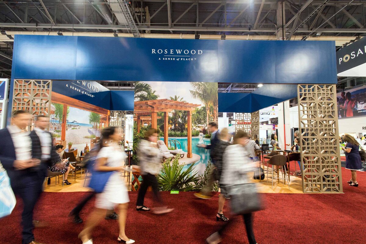 A crowd is blurred walking by the Rosewood booth at convention for event planners