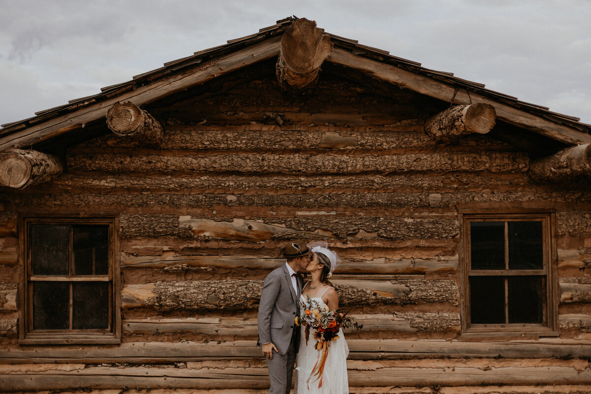 bride and groom standing outside of an old log cabin in the desert