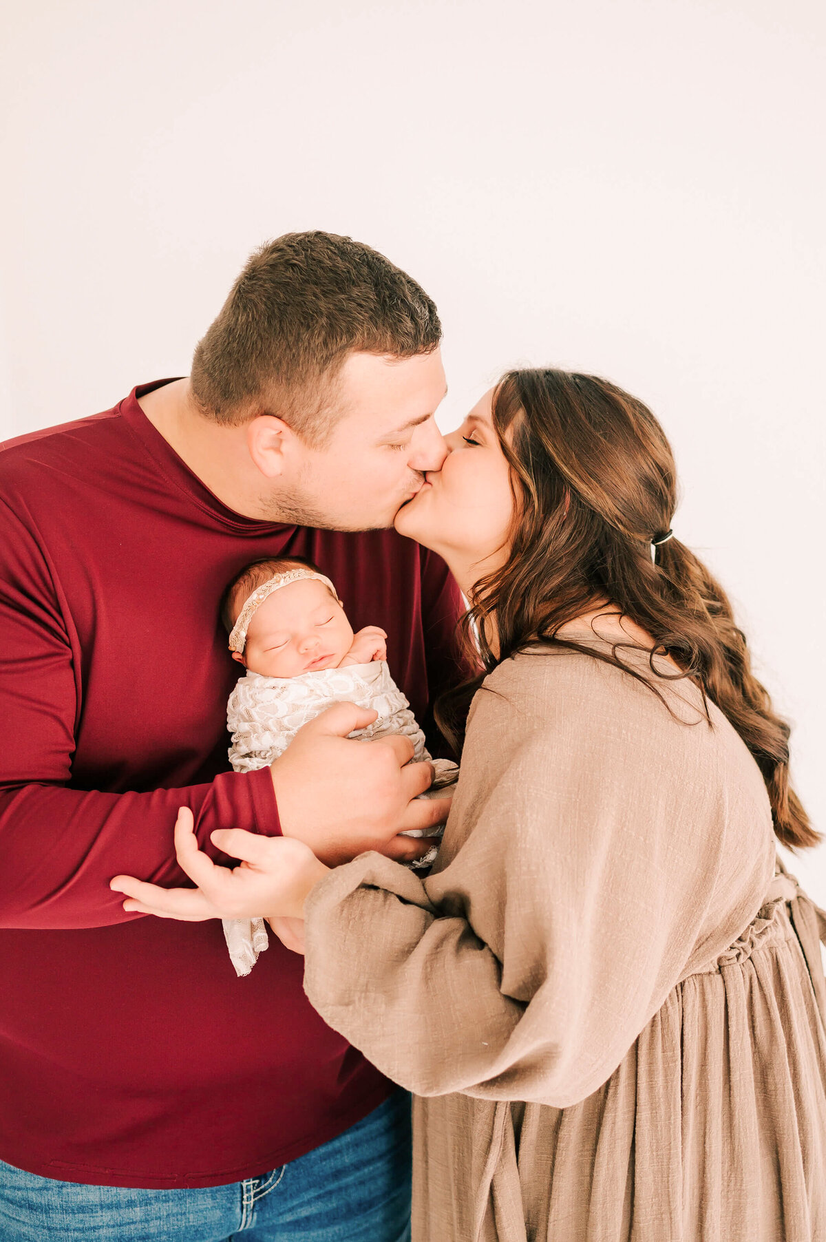 parents kissing holding baby girl in Springfield Mo newborn photography studio