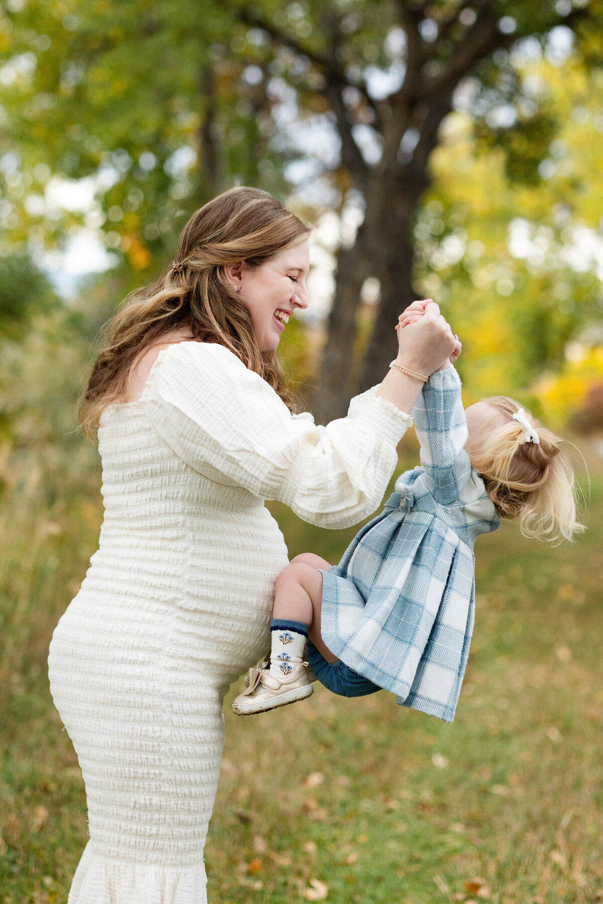 Mom smiling at and picking up her toddler daughter.