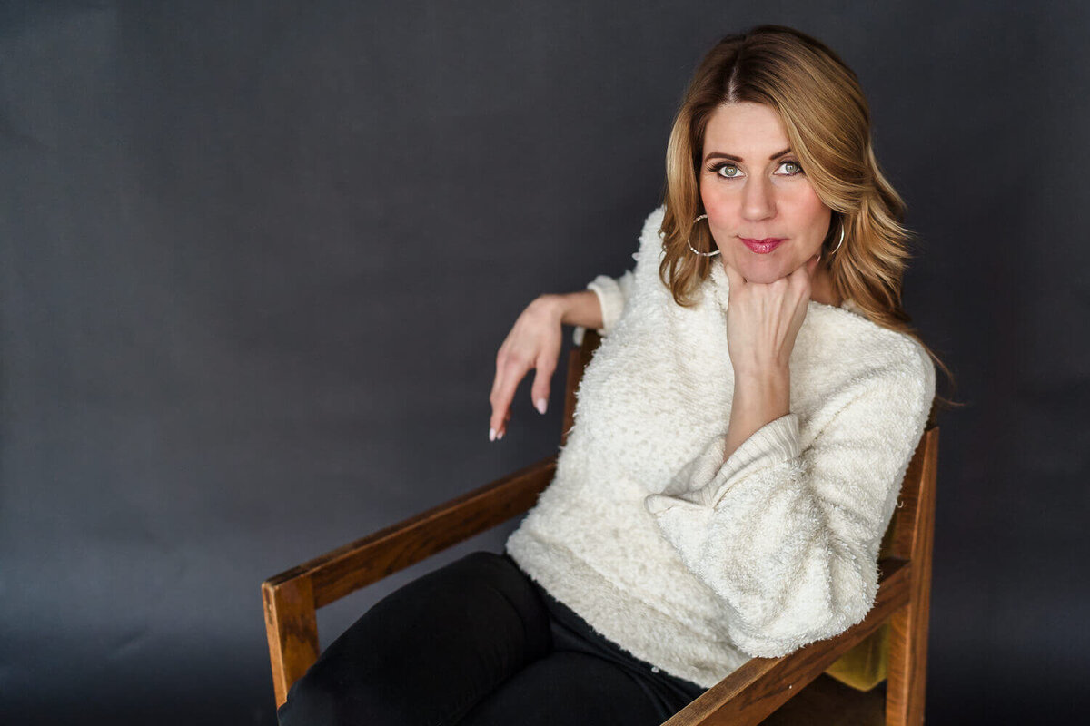 Woman in cream sweater sitting in chair leaning slightly forward for headshot photos