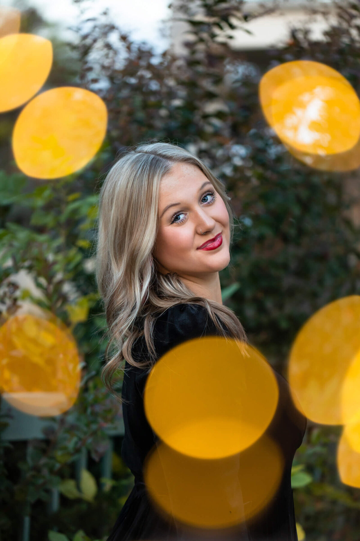 A unique and fun senior portrait of a blonde teen girl wearing a black dress is framed by golden light orbs. Captured by Springfield MO photographer Dynae Levingston