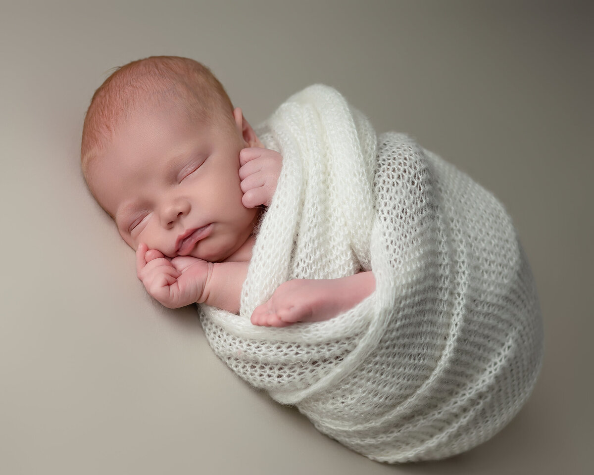 Baby sleeping in a studio in a white swaddle with a foot sticking out