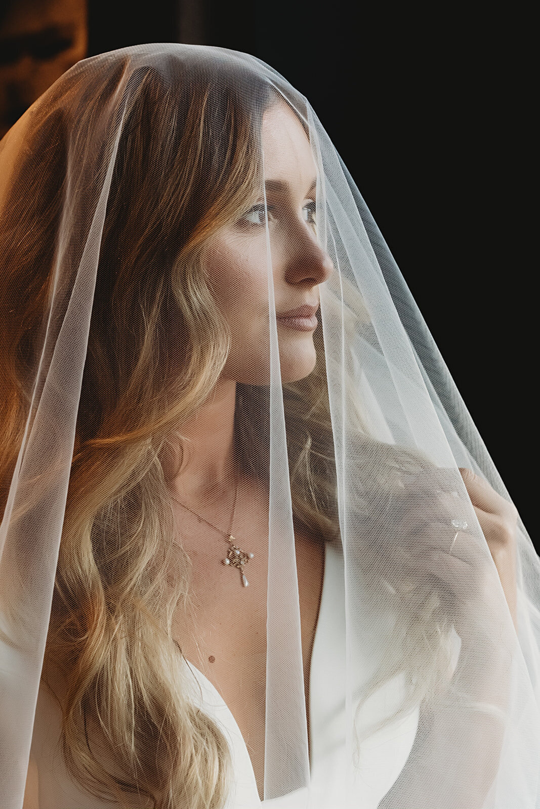 couture bride looks just over her shoulder as her veil graces her bombshell curled wedding hairstyle