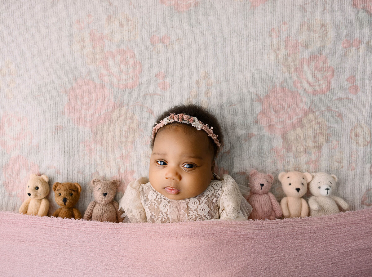 Newborn baby girl laying on a beautiful backdrop with teddy bears