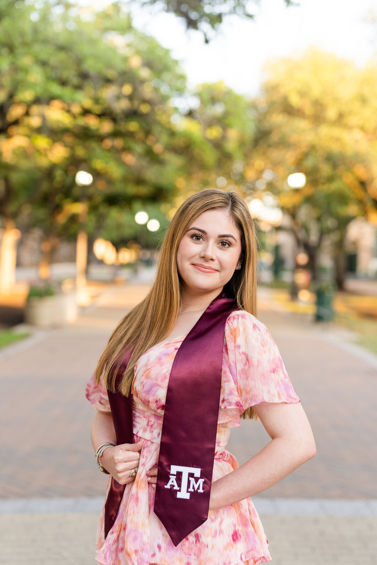 Texas A&M senior girl smiling in Military Plaza with a pink dress and maroon stole at sunset