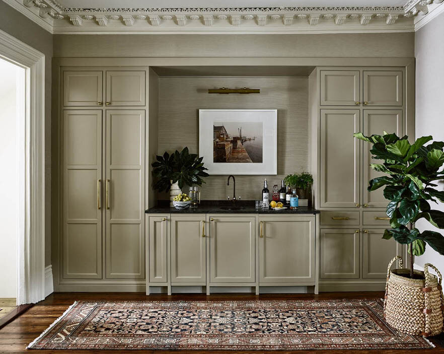 Light taupe cabinets match the grasscloth walls, offering dining storage, a guest coat closet, and a central wet bar with sink, ice machine, and beverage refrigerator. By Sarah Scales.