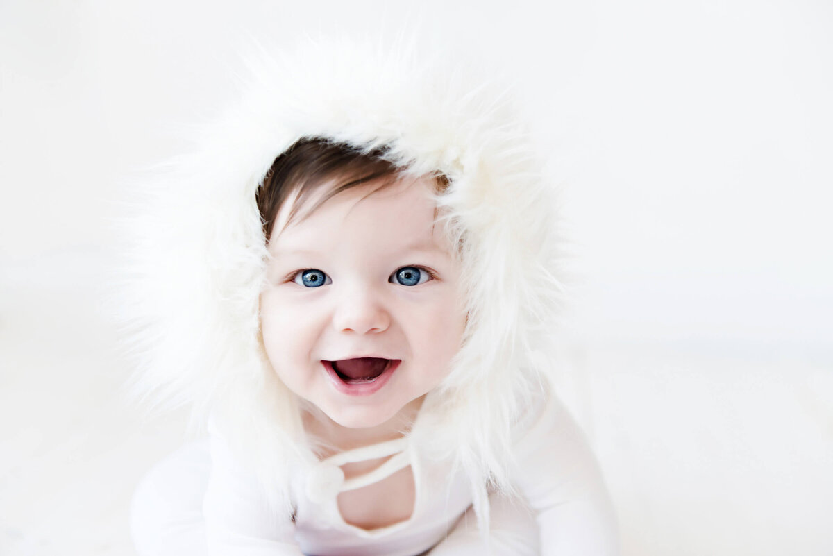 Baby with blue eyes wearing a furry hat for his kids portrait session in Burlington, ON