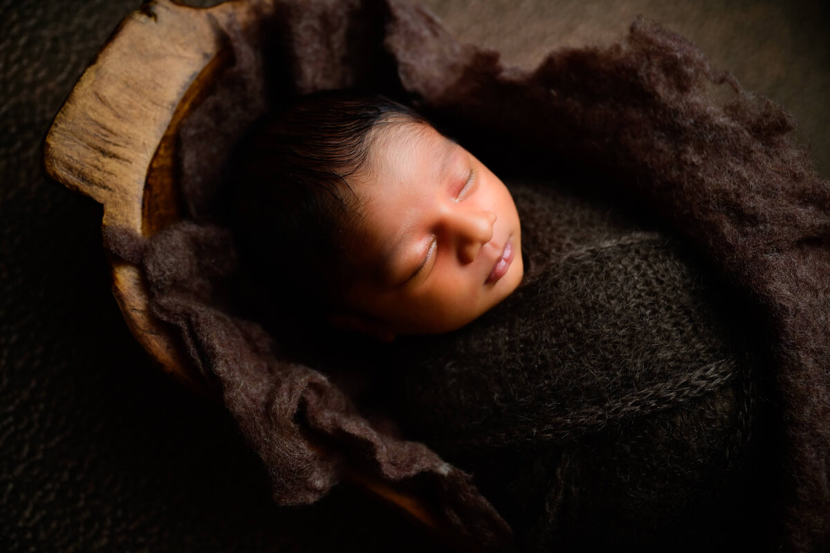 KItsap Peninsula newborn sleeping in large brown bowl while wrapped in brown on a  brown background .