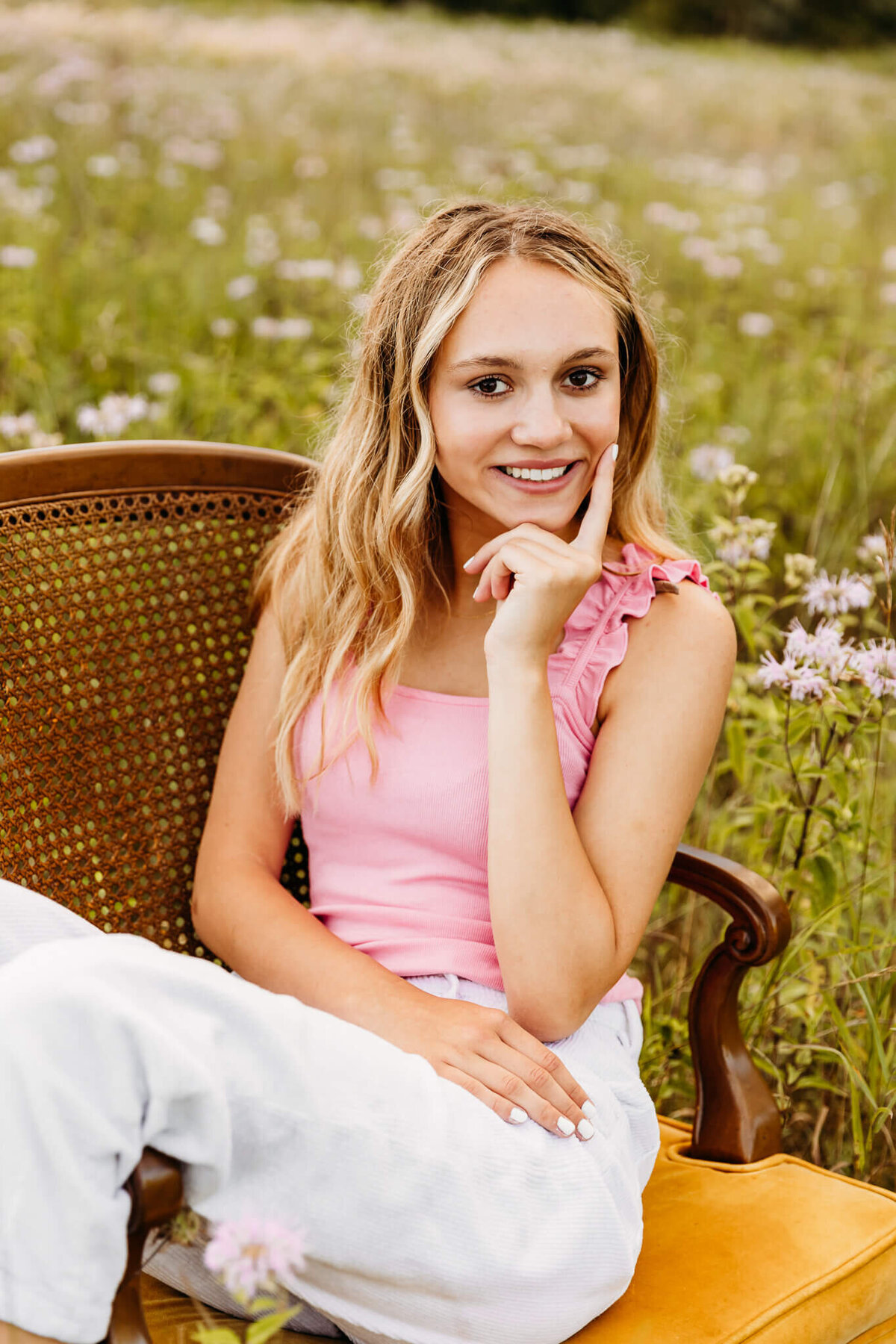 teen in pink tank top sitting in a yellow chair in a field of wildflowers