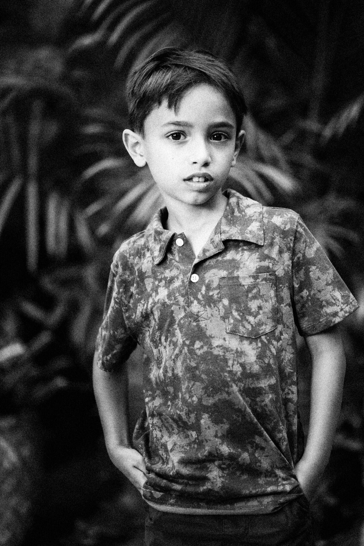 a young boy with his hands in his pockets in front of palm trees.