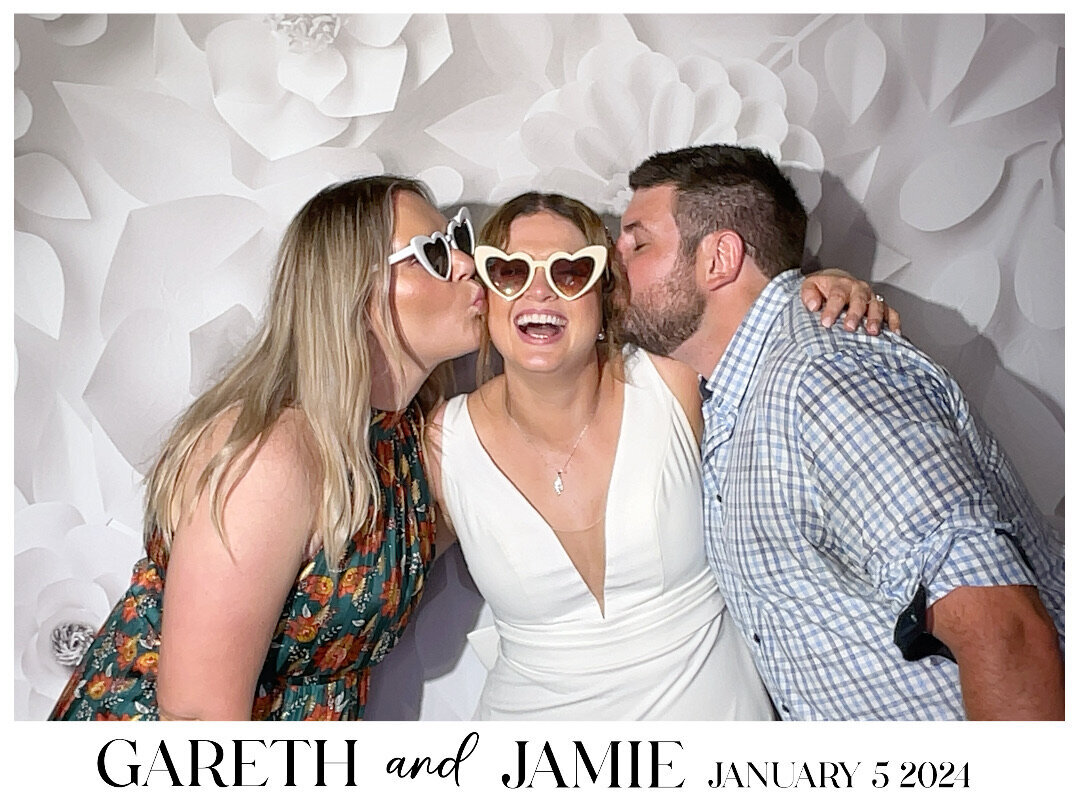 two wedding guests kiss brides cheek in photo booth capture on white floral background in christchurch