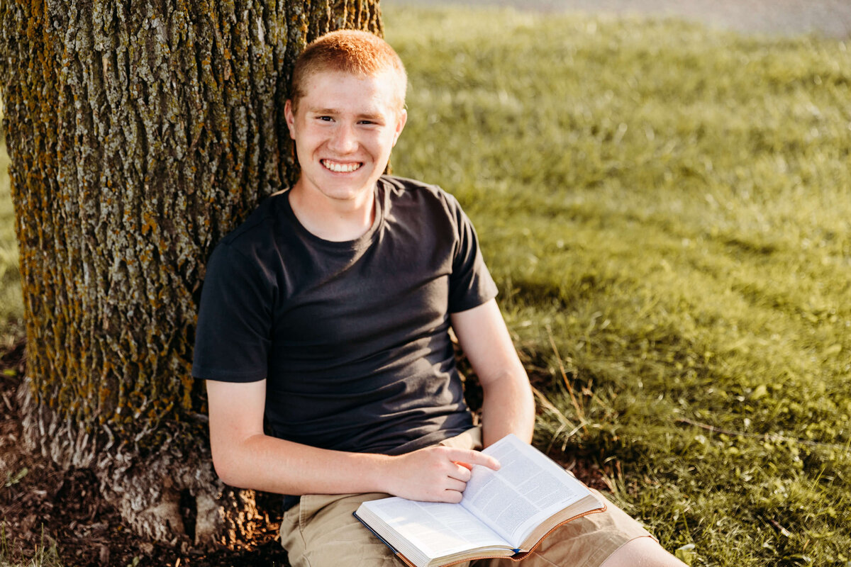 Young man reading by a tree during his senior photography session