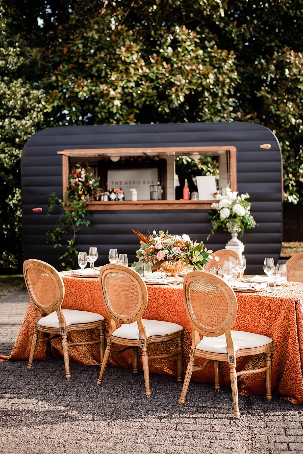 outdoor wedding table setting with floral centerpiece and bar trailer