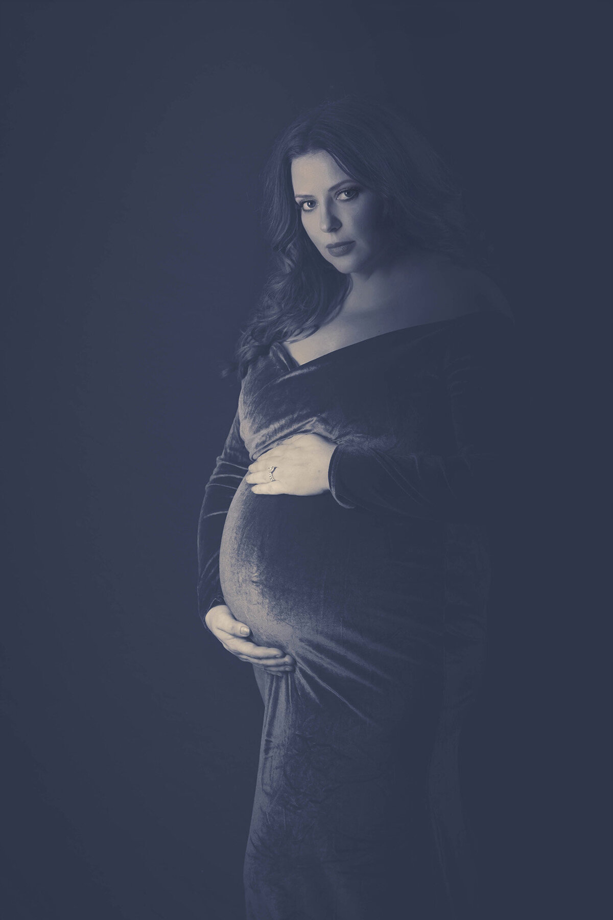 A black and white image of a woman in a velvet dress holding her bump