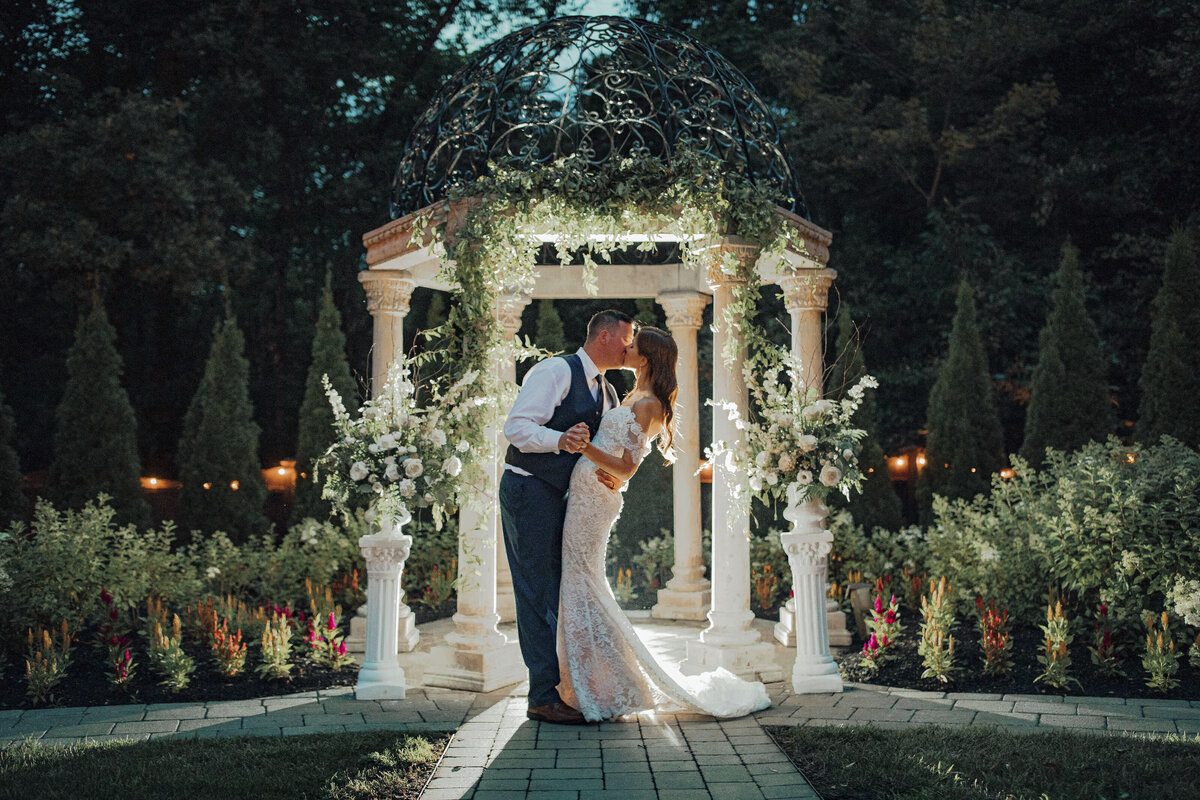 Hamilton Manor | Bride and groom kissing under gazebo with ivy and twinkle lights during summer wedding night | Hamilton Township, New Jersey
