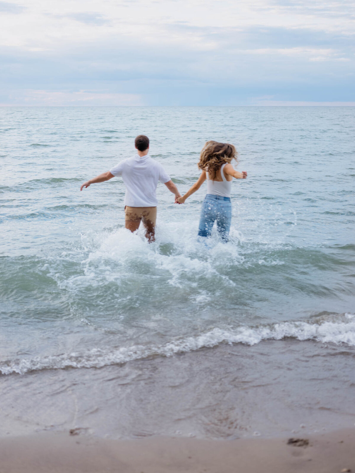 Engagement photo of a couple running into the water at the beach in Cleveland, Ohio.