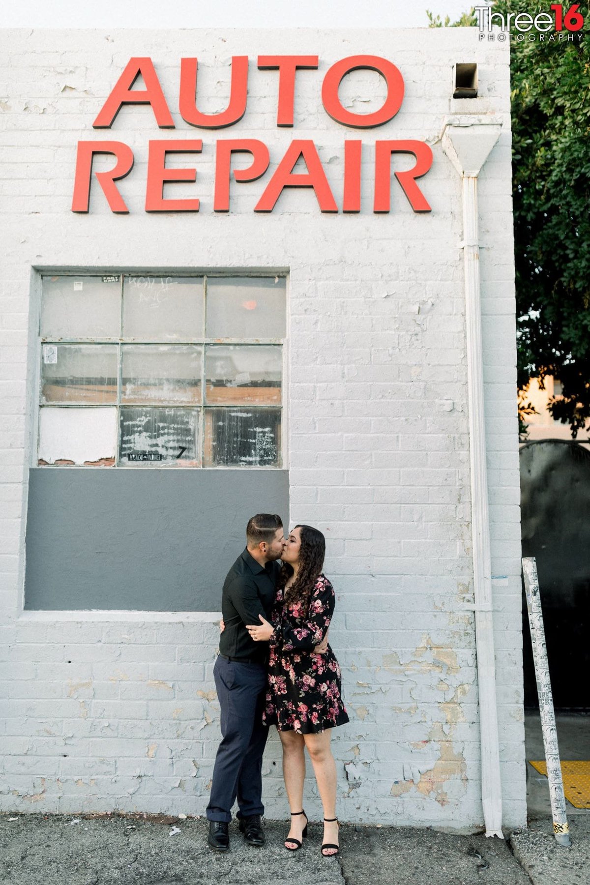 Engaged couple share a kiss under the Auto Repair sign