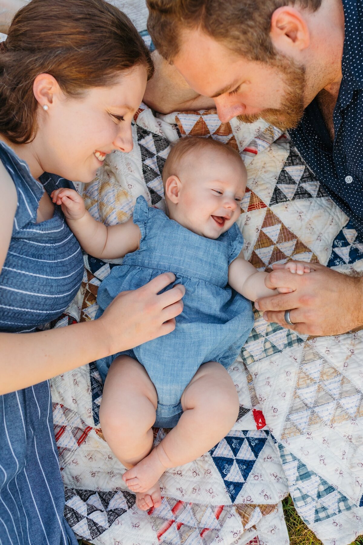 parents tickling their baby while laying on a picnic blanket