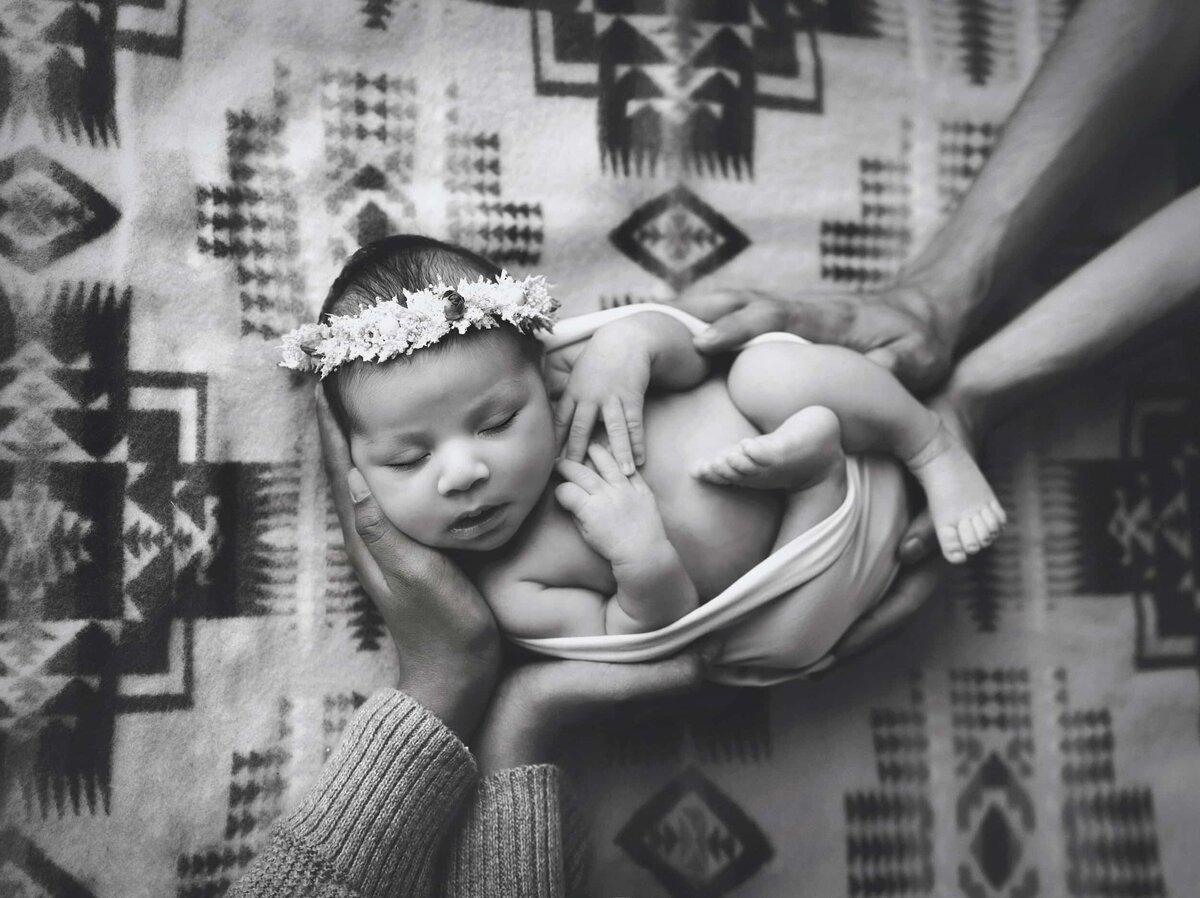 Black and white newborn portrait with parent's hands holding newborn