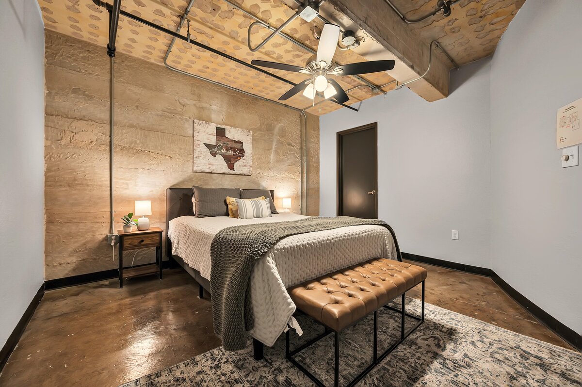 Bedroom with comfortable bedding in this one-bedroom, one-bathroom industrial vacation rental condo with free Wifi, onsite laundry, and space for four in the historic Behrens building of downtown Waco, TX.