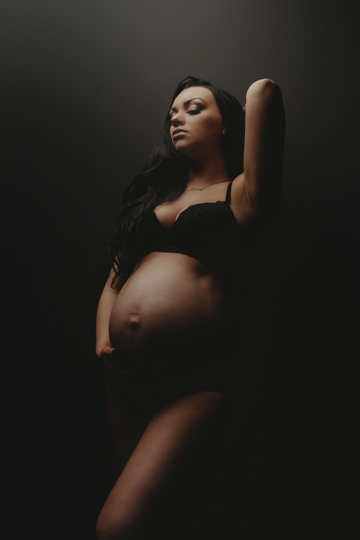 Pregnant lady wearing black bra and panties posed standing up showing off tummy