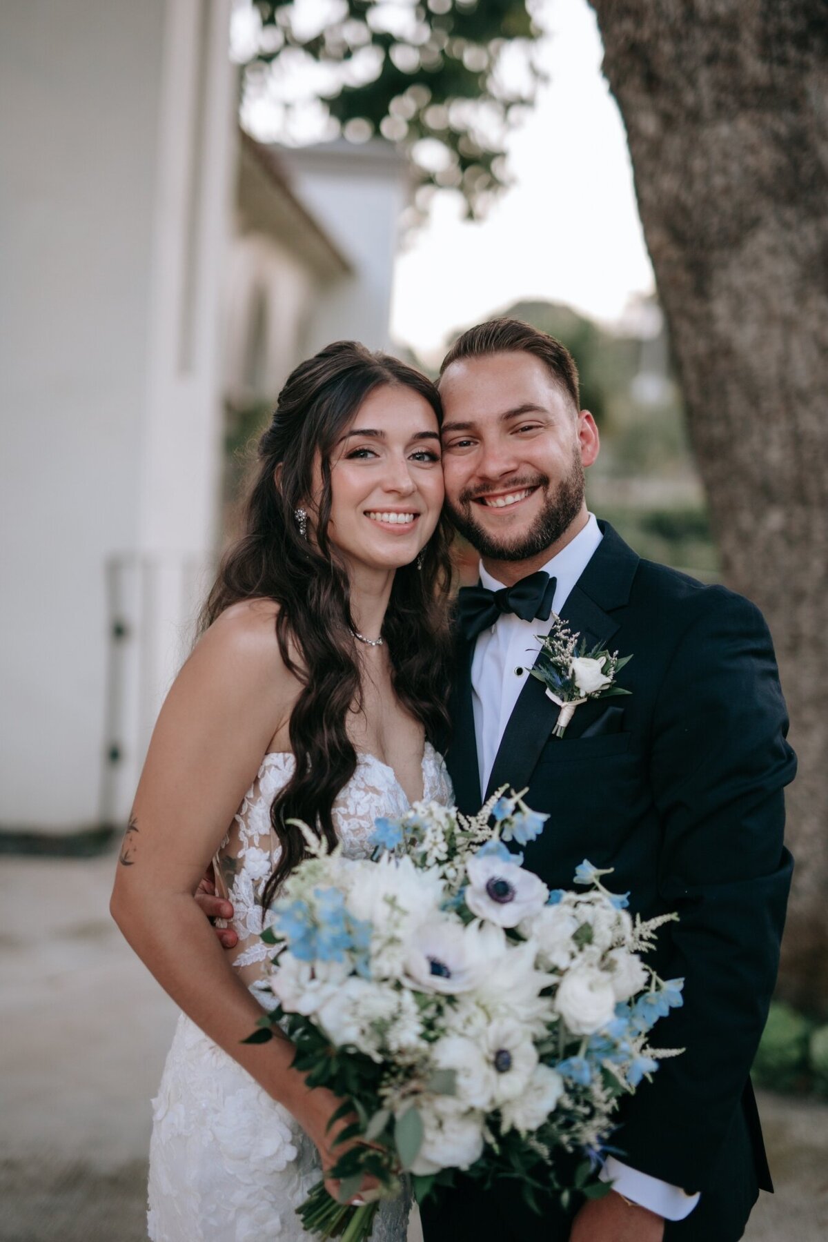 Bride and Groom smiling while bride holds her blue and white bouquet.