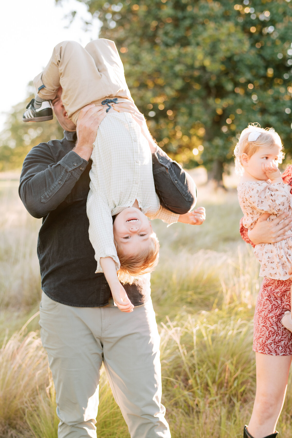 Dad holds son upside down and plays with him during a family session. Image by Raleigh maternity photographer A.J. Dunlap Photography.