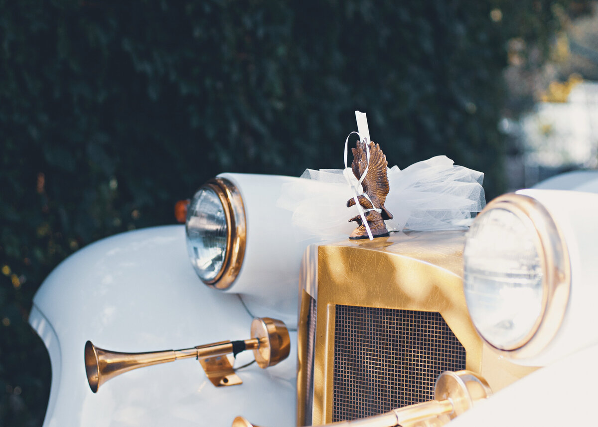 A close up image of the bonnet of a vintgaw white wedding car with a gold grill.