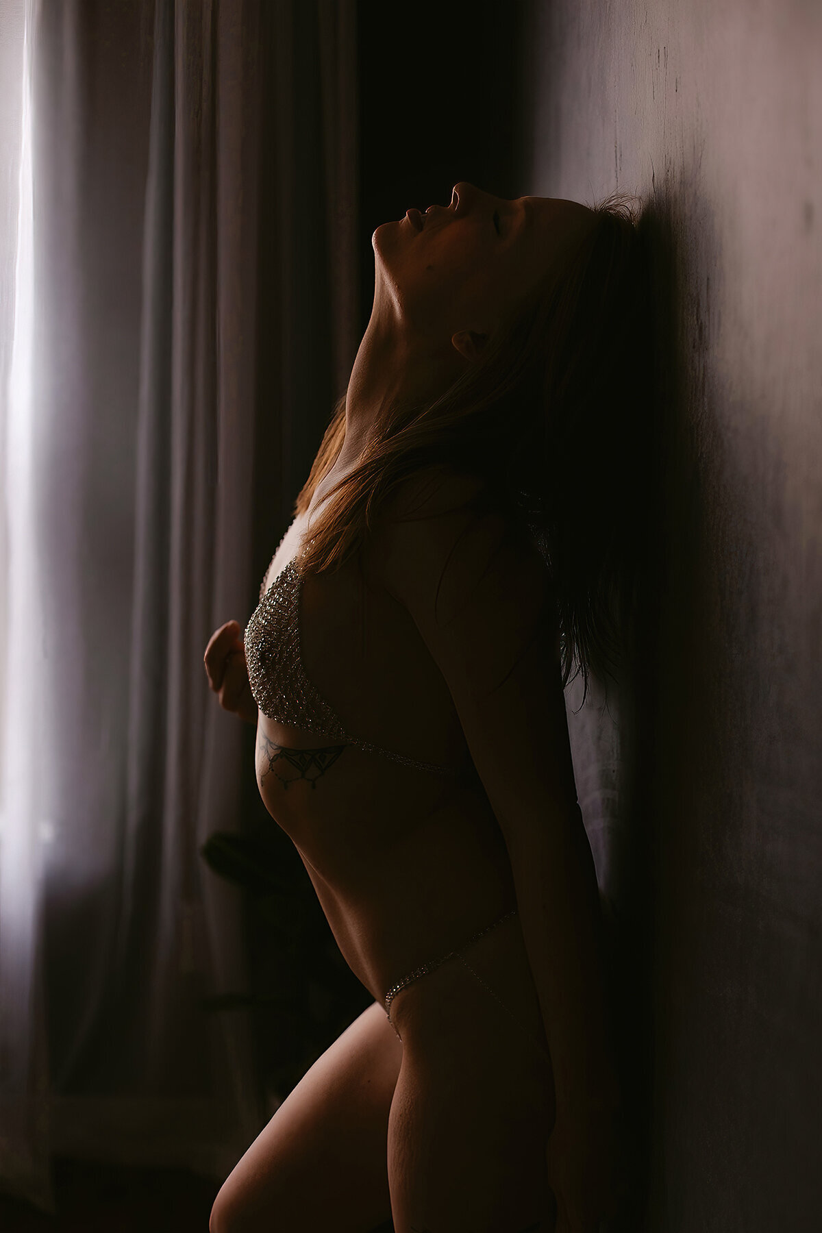 A woman in crystal lingerie leans seductively against a wall in a Bentonville boudoir photoshoot.