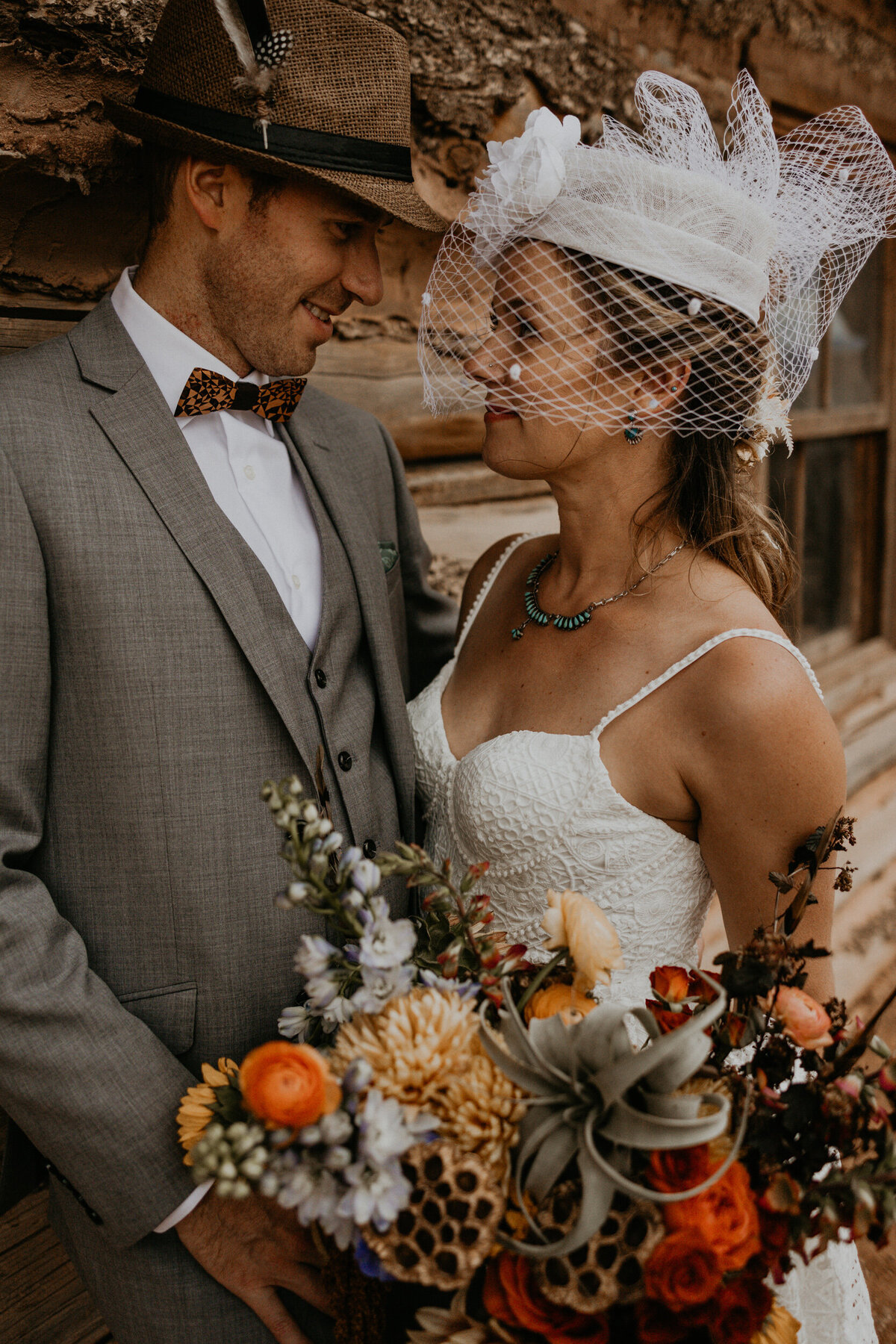 bride and groom standing outside of an old log cabin in the desert