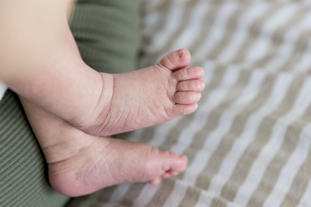 Close-up of a baby's tiny feet crossed over each other on a striped bedsheet.