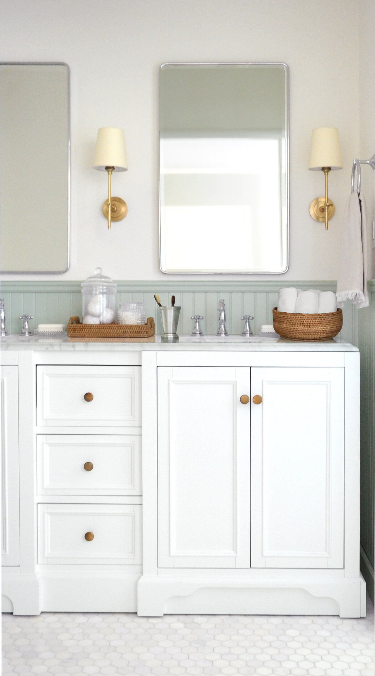 White vanity with sink and rattan countertop accessories, brass sconces and mirrors