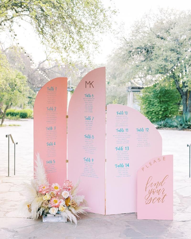 Wedding reception seating chart backdrop made of pink arches and blue letters and decorated with floral arrangements