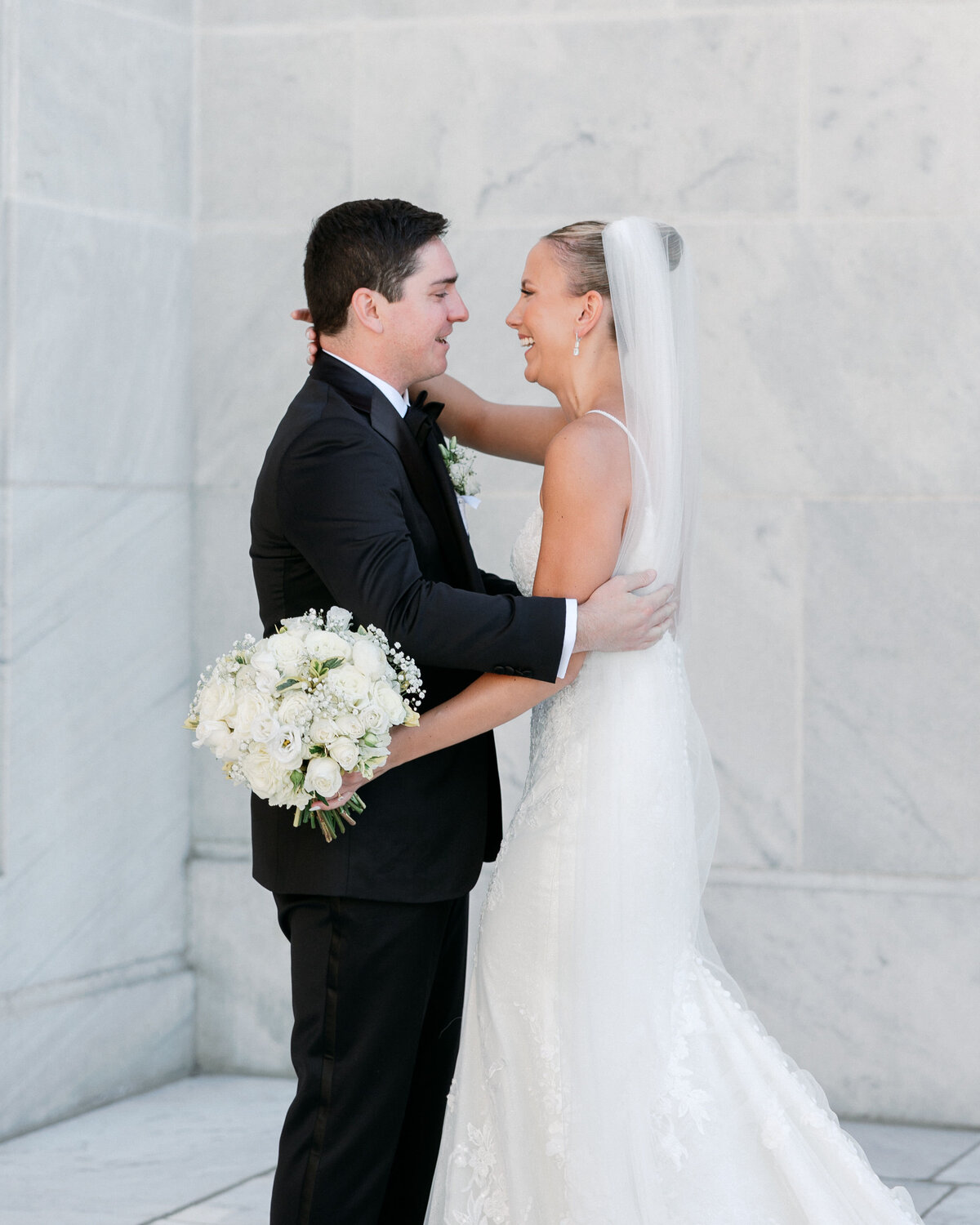 Bride and groom embrace joyfully during first look outside a marble building in Philadelphia.