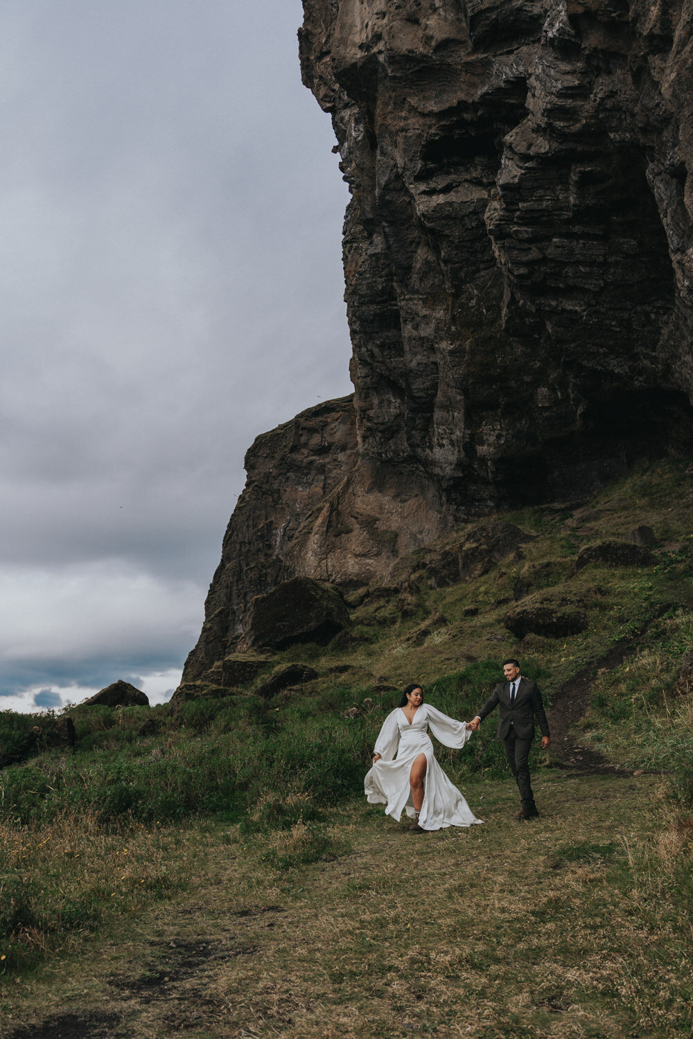 Husband and wife walk down the mountain with the bride's dress blowing in the wind 