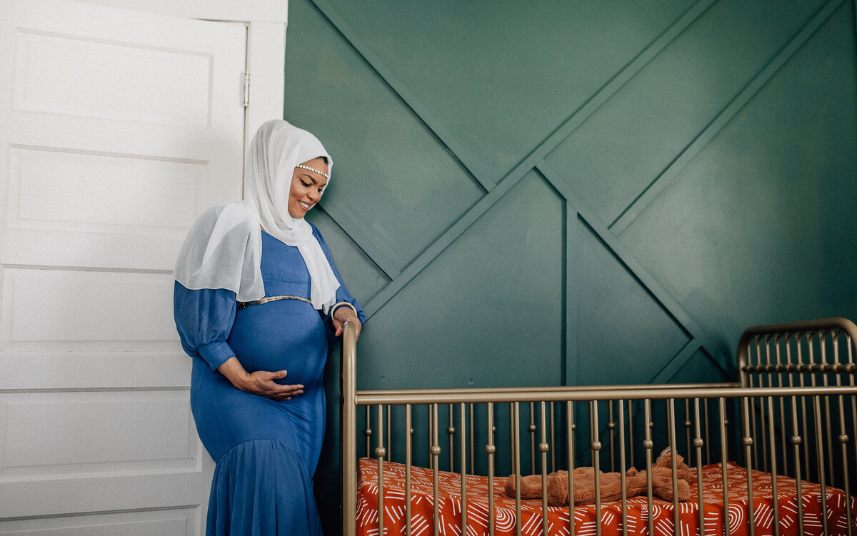 Maternity photoshoot with woman standing next to a crib.