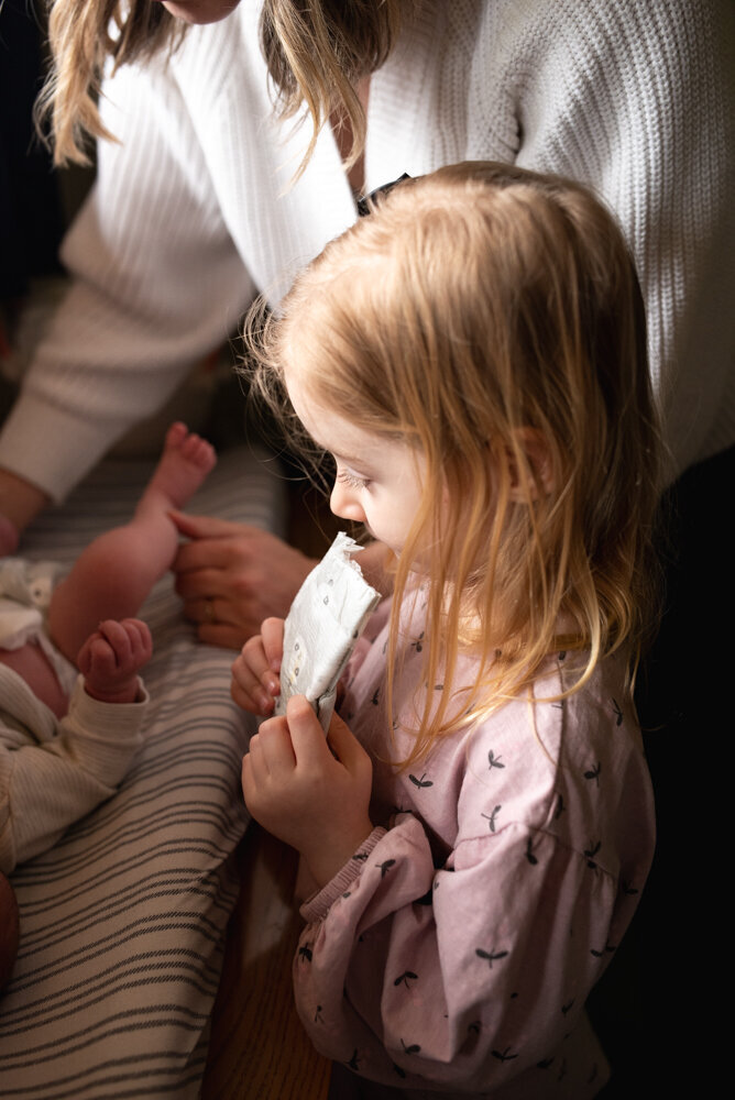 Big sister eagerly waiting to help mom with baby brother's diaper change