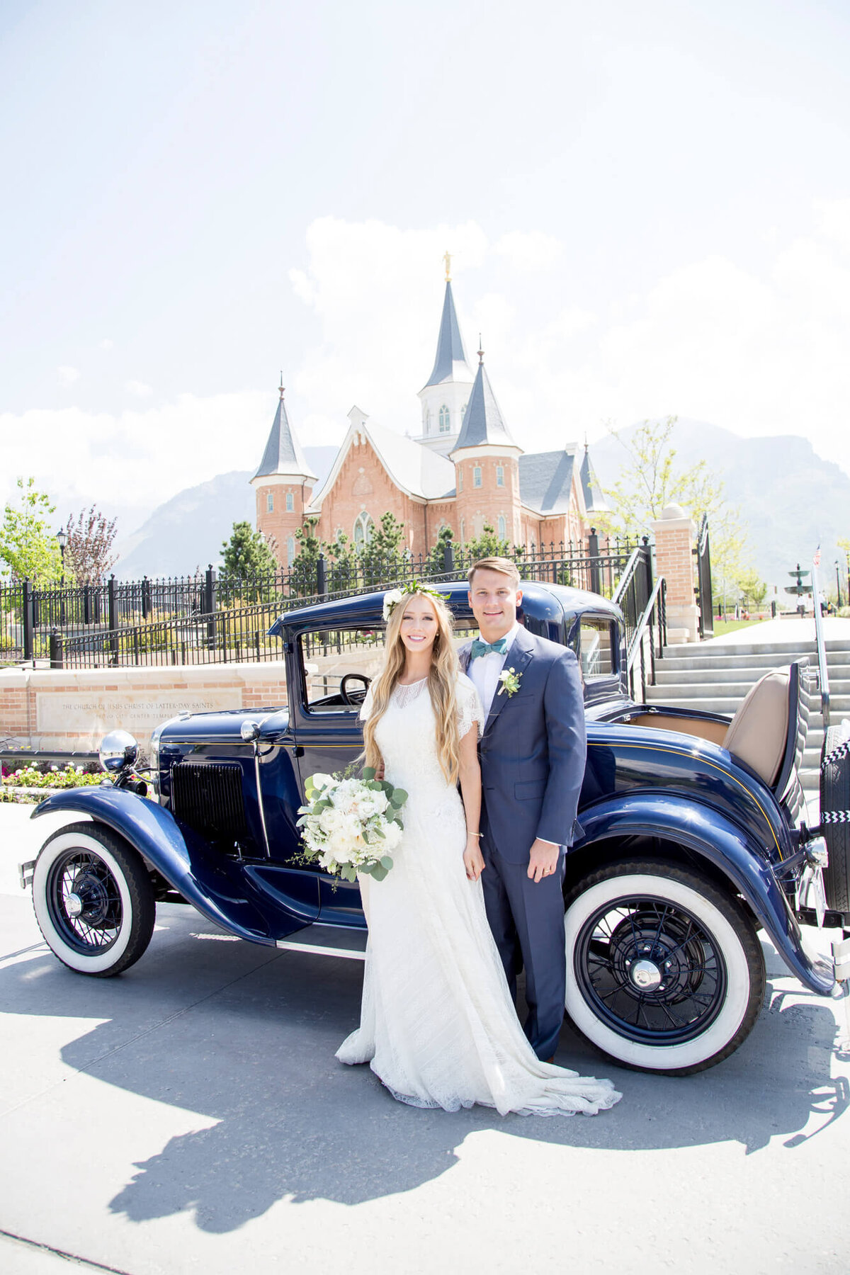 a bride and groom posing in front of a blue vintage car by  a brick building, wedding photogrpahy by Jessica Bowles